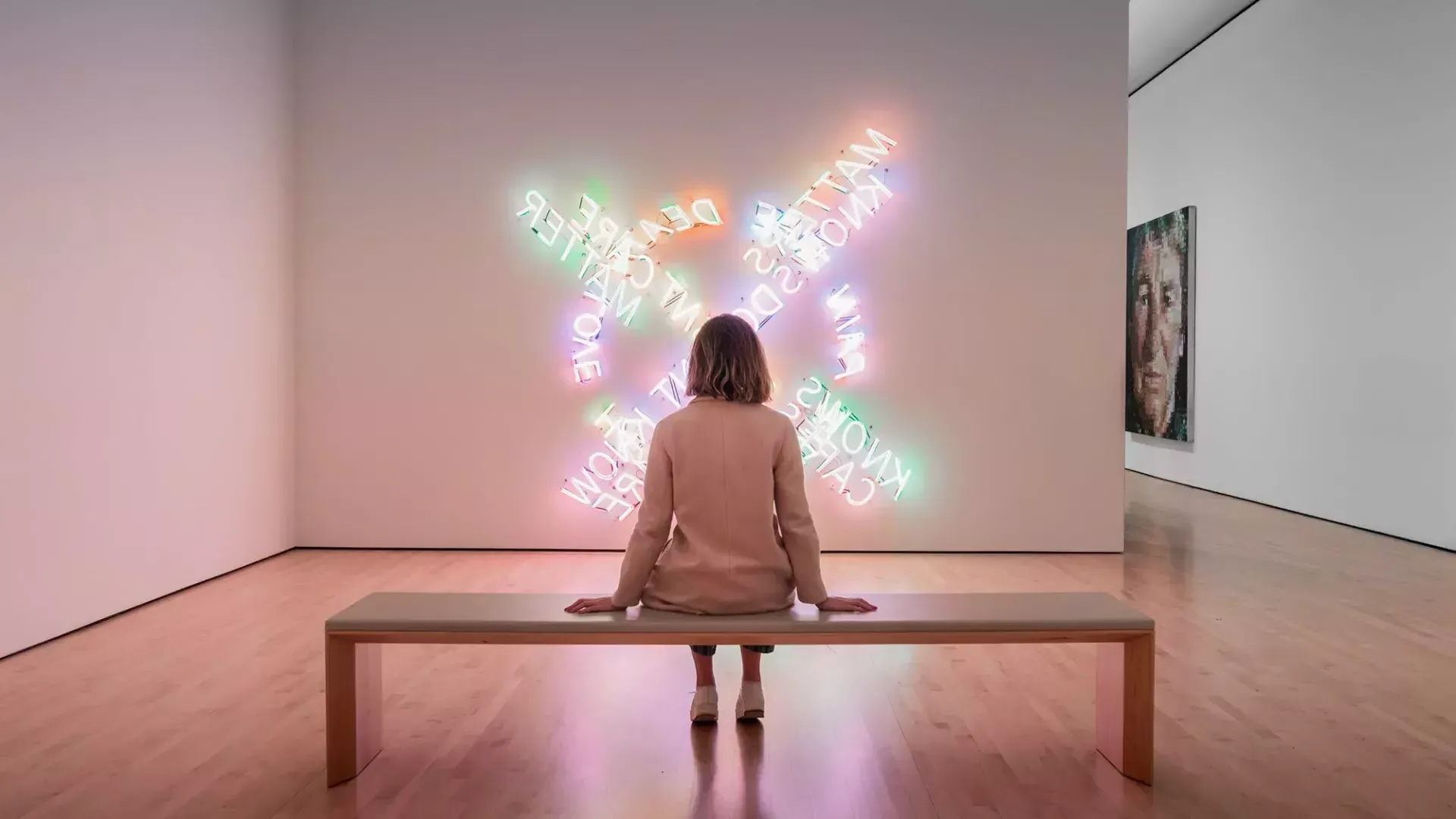 Une femme, assise sur un banc, regarde une œuvre d’art lumineux contemporain au SF MOMA à San Francisco.